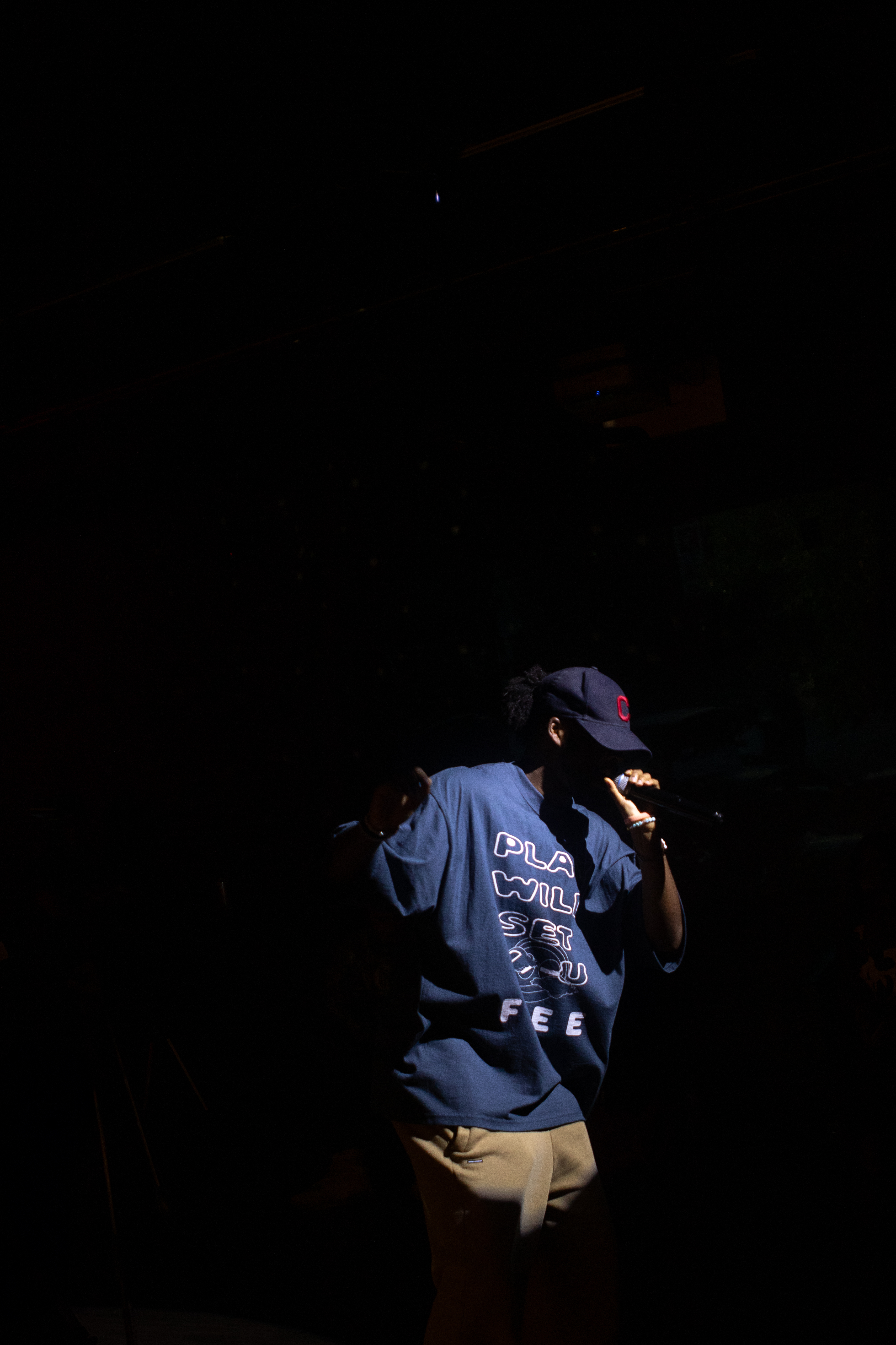 Stage shot of the PWSYF tee from behind, lit by a single spotlight